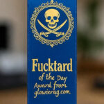 Official Glowie Rag “Fucktard of the Day” blue ribbon award with gold text and skull emblem – presented to the most brain-dead politician, activist, or media clown of the day.